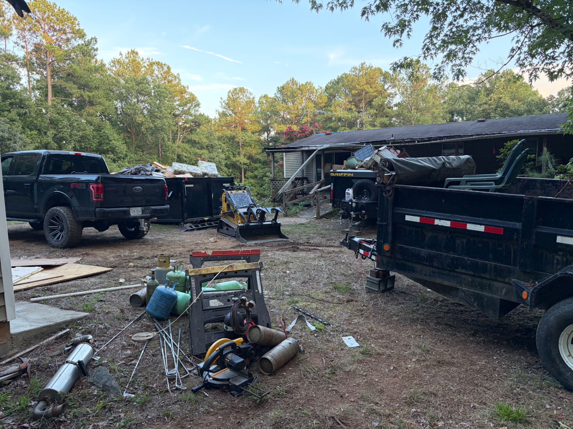 Loaded dump trailer, skid steer and sorted debris during a property cleanout